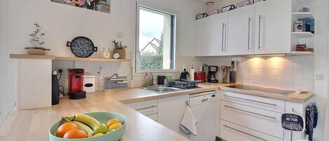 Une cuisine moderne avec des meubles blancs, un plan de travail en bois et un saladier rempli de fruits.