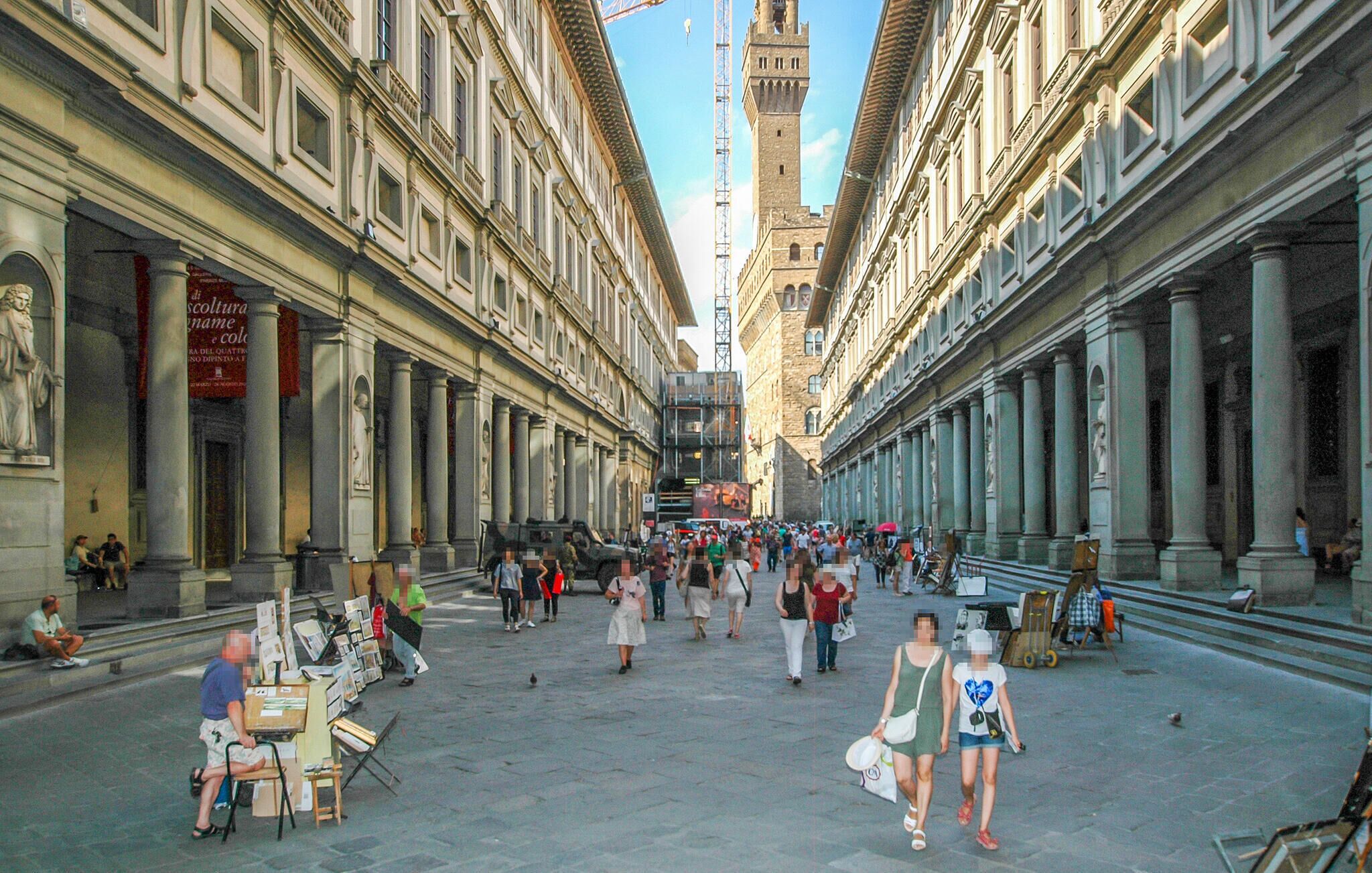 A bustling street with historic buildings, a prominent tower, and a market area.