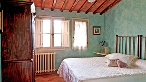 A bedroom with a wooden ceiling, two windows with white shutters, a radiator, a bed with a white quilt, a nightstand with a vase, and a picture on the wall. - Stunning home in Montelupo Fiorentino (Montelupo Fiorentino)