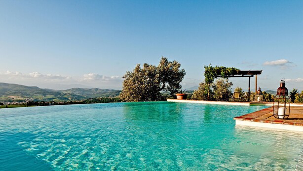 A clear blue infinity pool with a view of distant hills, a pergola with seating, and a lantern. - Stunning home in Montelupo Fiorentino (Montelupo Fiorentino)