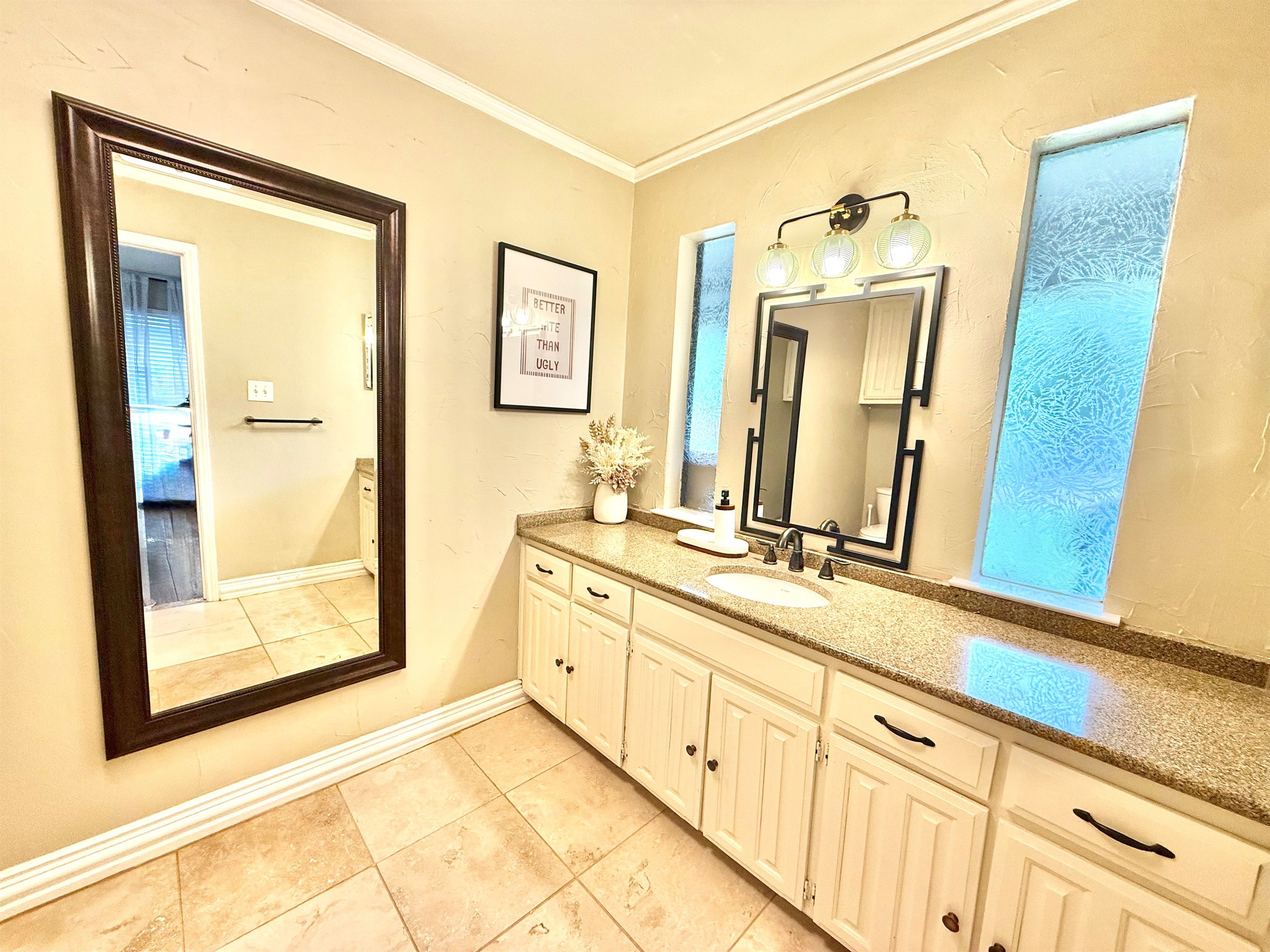 A bathroom with a large mirror, vanity with a sink, and a framed motivational quote on the wall.