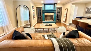 A living room with a sofa, a coffee table, a fireplace, and a dining area. - Summer Oasis - Pool and Hot Tub, Private Backyard (Keller)