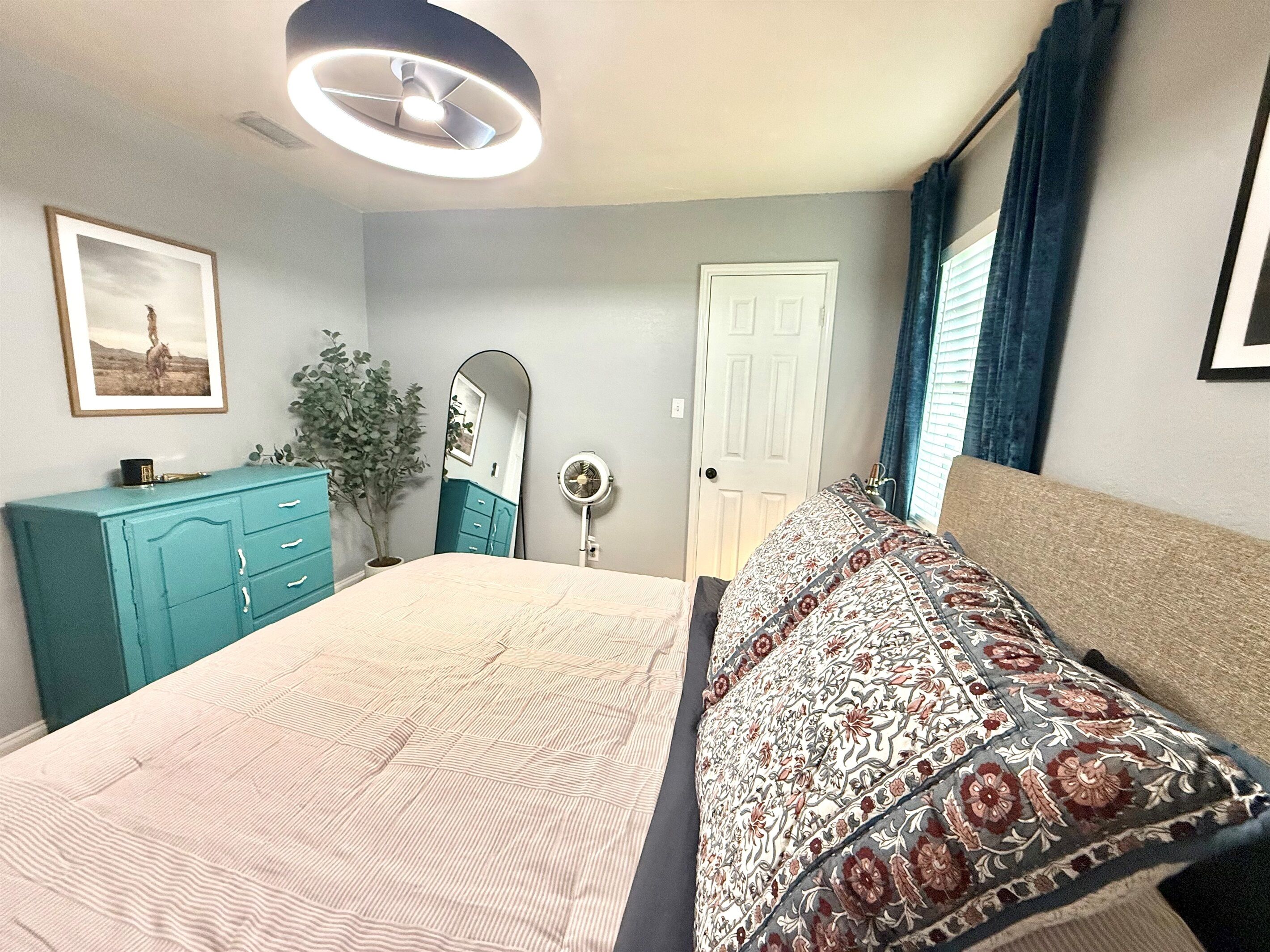 Une chambre à coucher avec un lit, une commode, un miroir, une porte et un ventilateur de plafond.