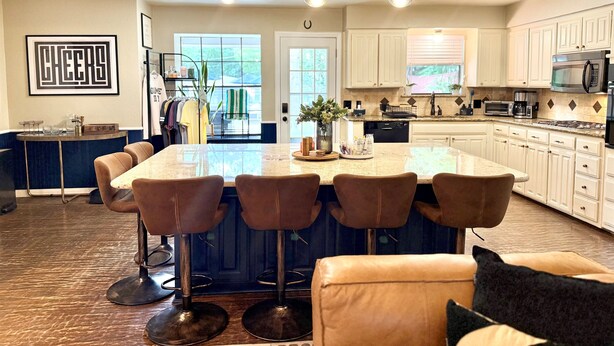 A modern kitchen with a central island, bar stools, and white cabinetry. - Summer Oasis - Pool and Hot Tub, Private Backyard (Keller)