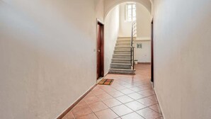 A narrow hallway with a tiled floor, a wooden door, and a staircase leading to an upper level. - Appartamento Camilla - Affitti Brevi Italia (Lucca)