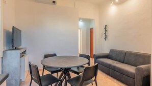 A modern living room with a round table and chairs, a grey sofa, and a flat-screen TV on a stand. - Appartamento Camilla - Affitti Brevi Italia (Lucca)