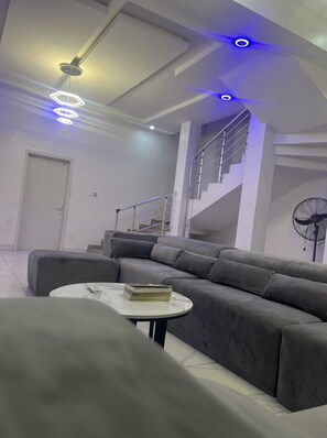 Relax in this stylish living room with a comfortable sofa and coffee table, featuring a staircase leading to an upper level and a unique ceiling design.