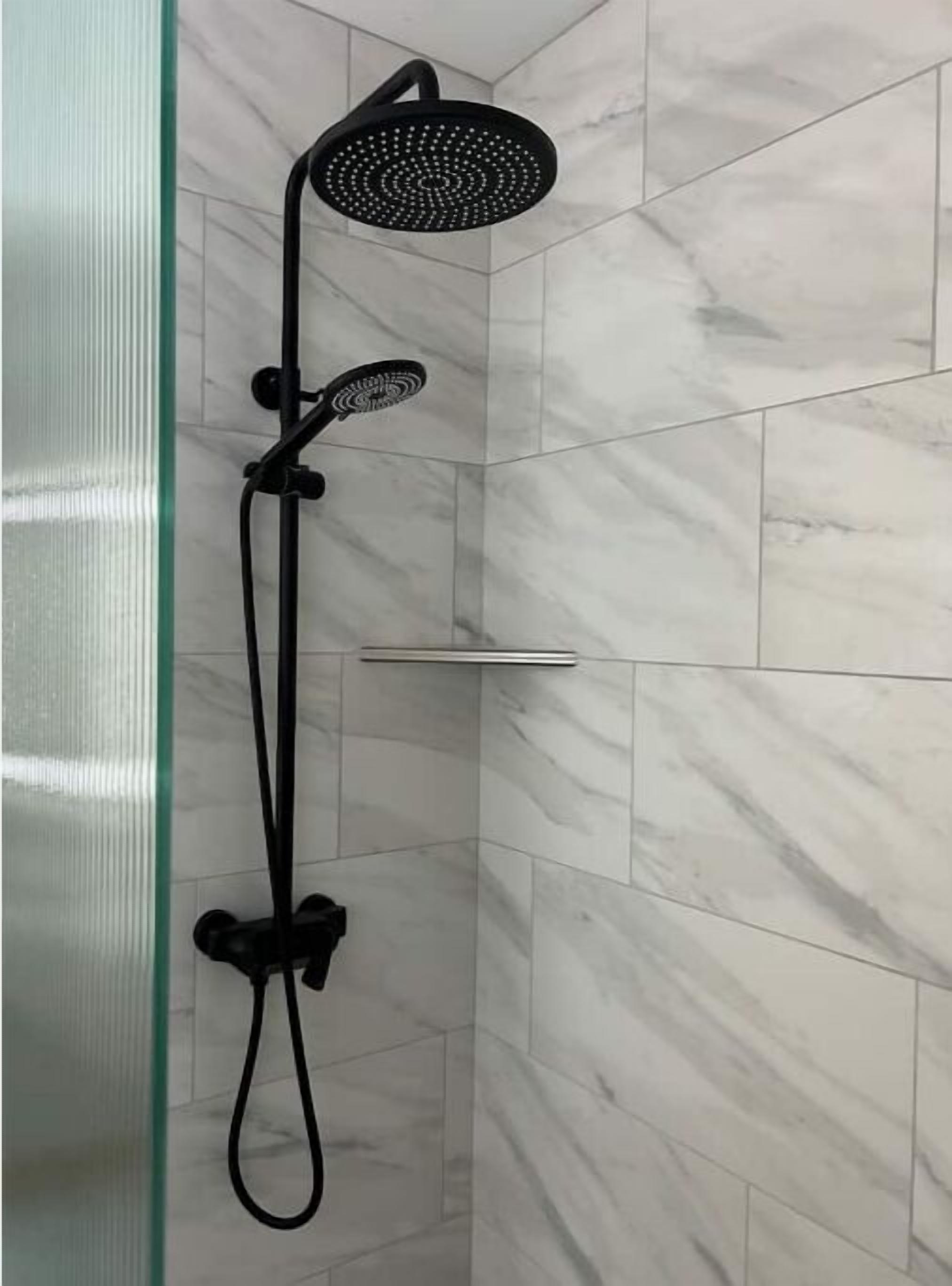 A black showerhead with a handheld attachment, mounted on a wall with white marble tiles.