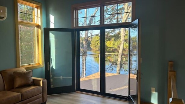 A room with a large sliding glass door leading to a lake view, a brown leather sofa, and a wooden floor. - Little cabin (Rhinelander)