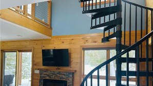 A spacious living area with a stone fireplace, a large flat-screen TV, and a wooden staircase. - Little cabin (Rhinelander)