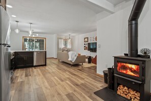 A modern living room with a wood-burning stove, a sofa, a dining area, and a kitchen. - Elk Park Retreat - A Comfy & Stylish Mt. Hood Cabin - Hot Tub, Dogs OK (Mount Hood Village)