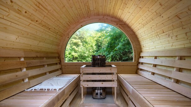 Una baita di legno con un'ampia finestra ad arco, un letto e un termosifone.