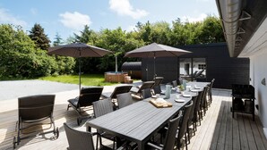 Patio esterno con un tavolo lungo e sedie, due ombrelloni e una vasca idromassaggio.