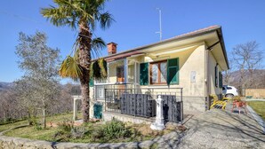 A single-story house with a balcony, a palm tree, and a mountain backdrop. - 2 bedroom cozy home in Varese Ligure (Varese Ligure)