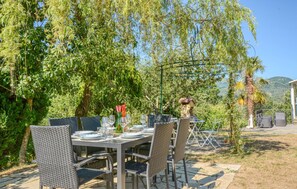 An outdoor dining area with wicker chairs and tables set up under a tree, surrounded by lush greenery and a mountain view. - 2 bedroom cozy home in Varese Ligure (Varese Ligure)