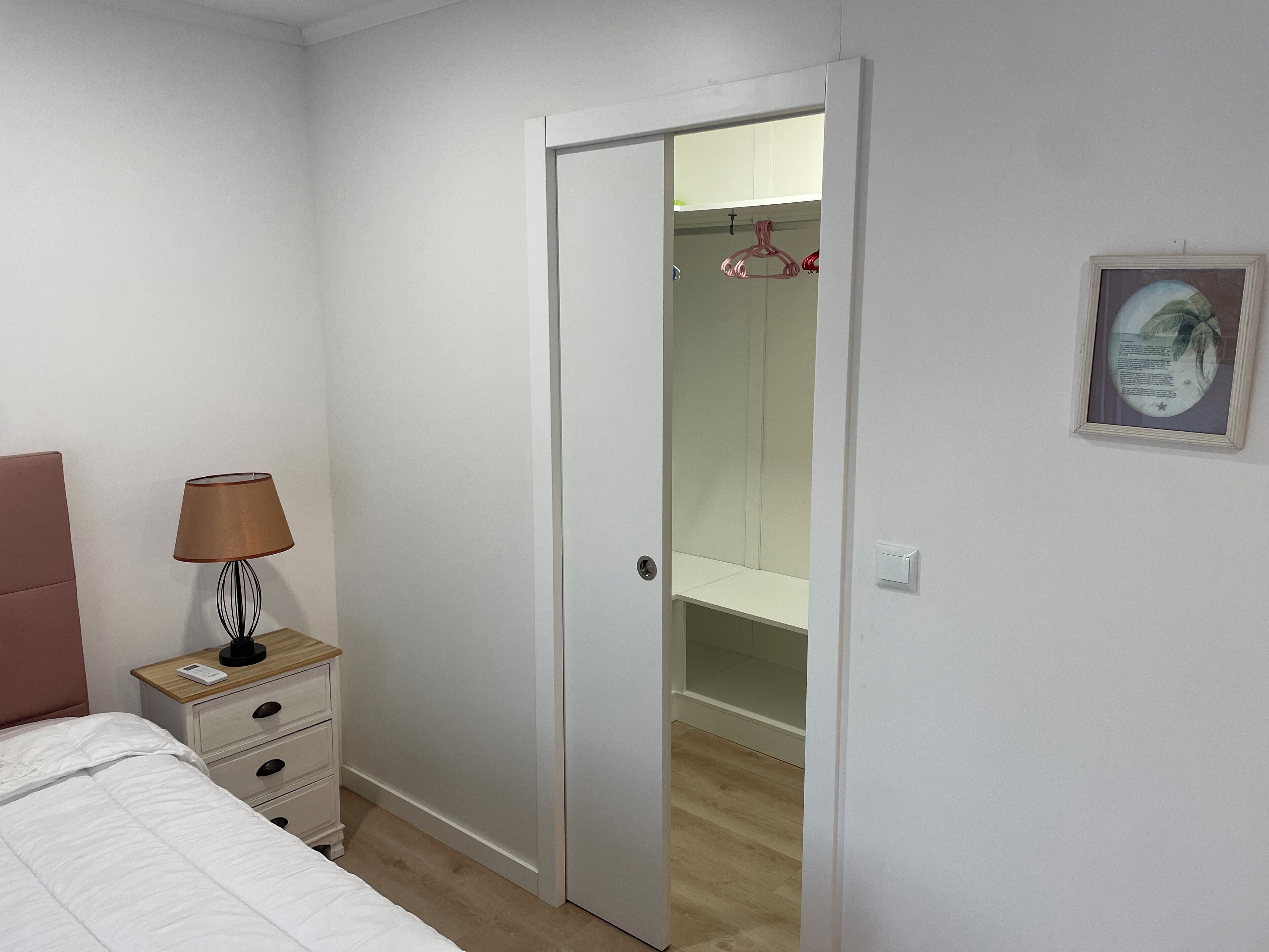 Une chambre à coucher avec un lit, une table de chevet avec une lampe, une armoire et un tableau encadré au mur.