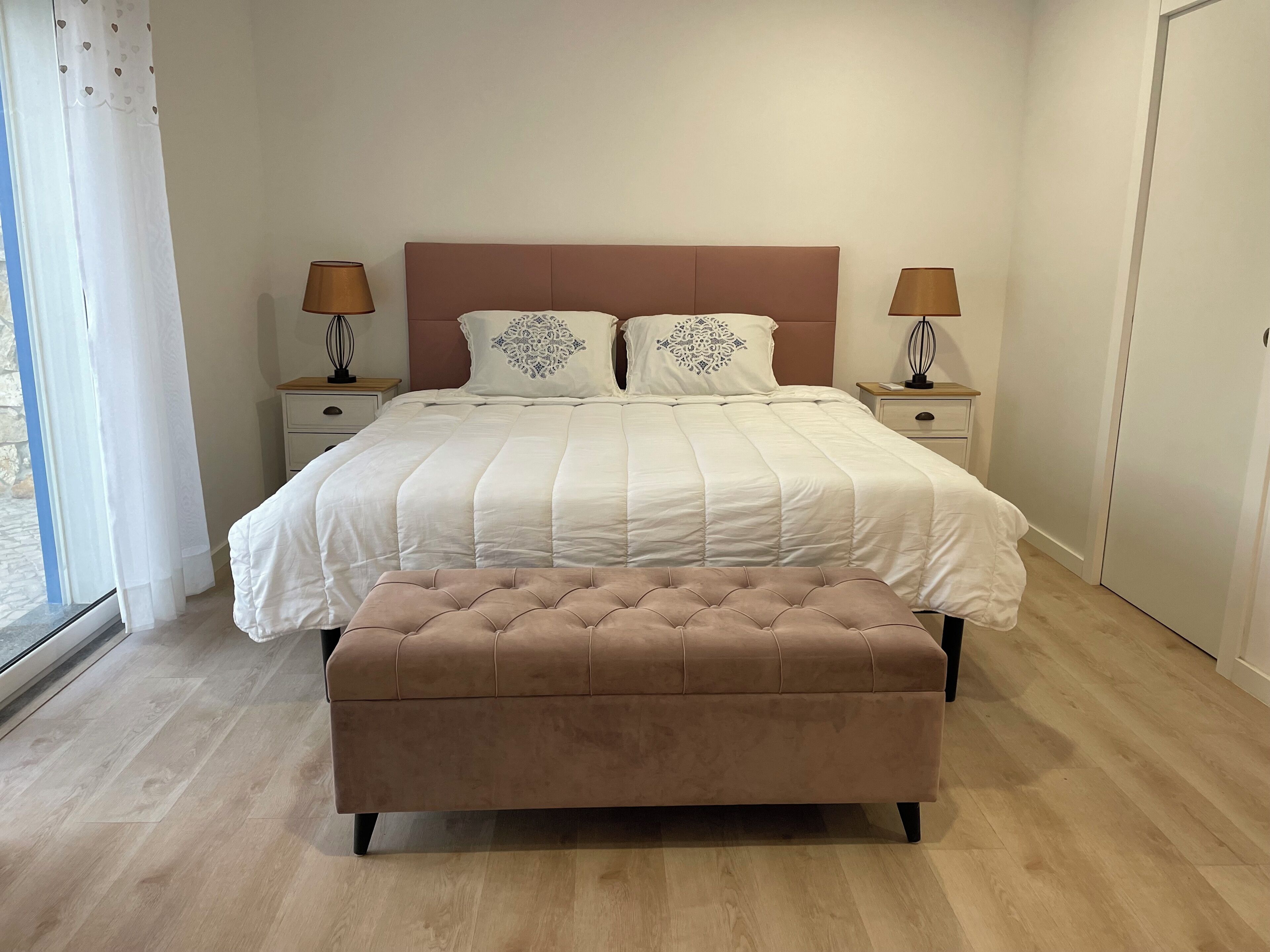 Ein Schlafzimmer mit einem Bett, zwei Nachttischen, einem Fenster mit Vorhängen und einem Holzboden.
