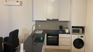 A compact kitchen with white cabinets, a built-in oven, a microwave, and a washing machine.