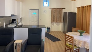 A compact kitchen with a coffee machine, a refrigerator, and a dining area with a table and chairs.
