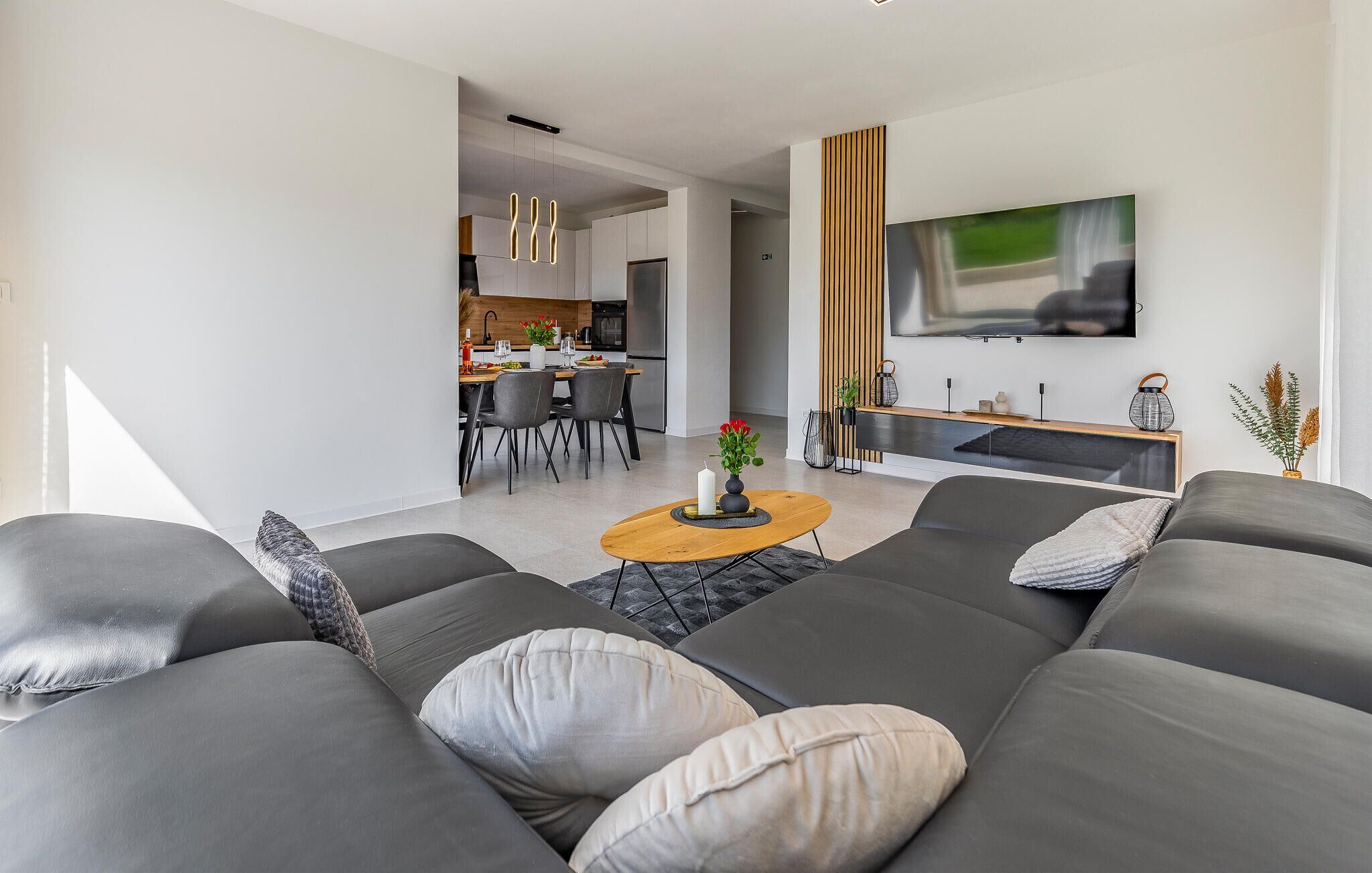 A modern living room with a grey sofa set, a wooden coffee table, and a flat-screen TV mounted on the wall.