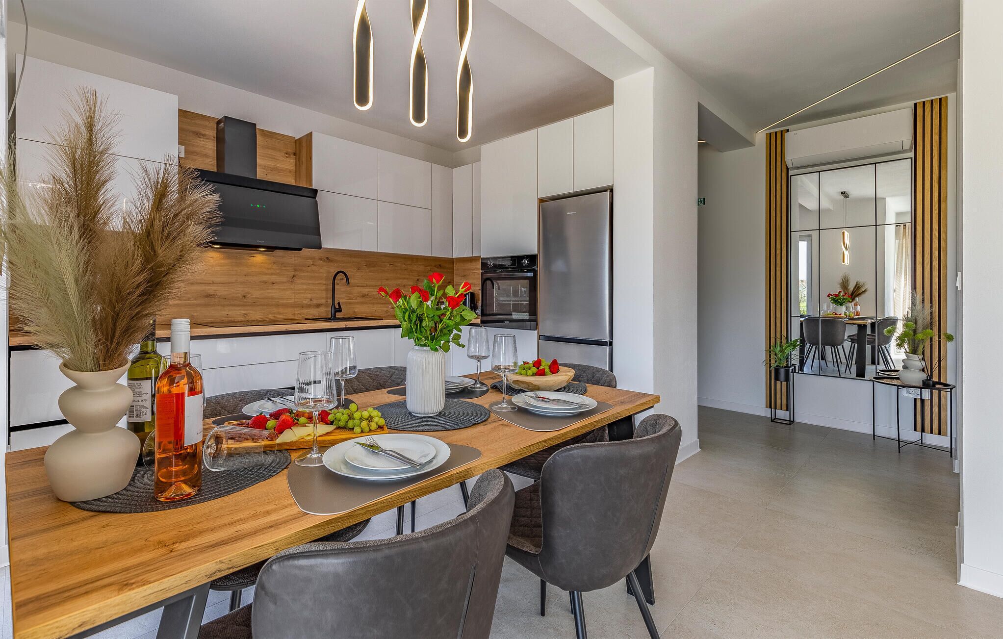 A modern kitchen with a wooden dining table, chairs, and a central island with a vase of flowers.