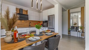 A modern kitchen with a wooden dining table, chairs, and a central island with a vase of flowers. - 2 bedroom gorgeous apartment in Pula (Pula)