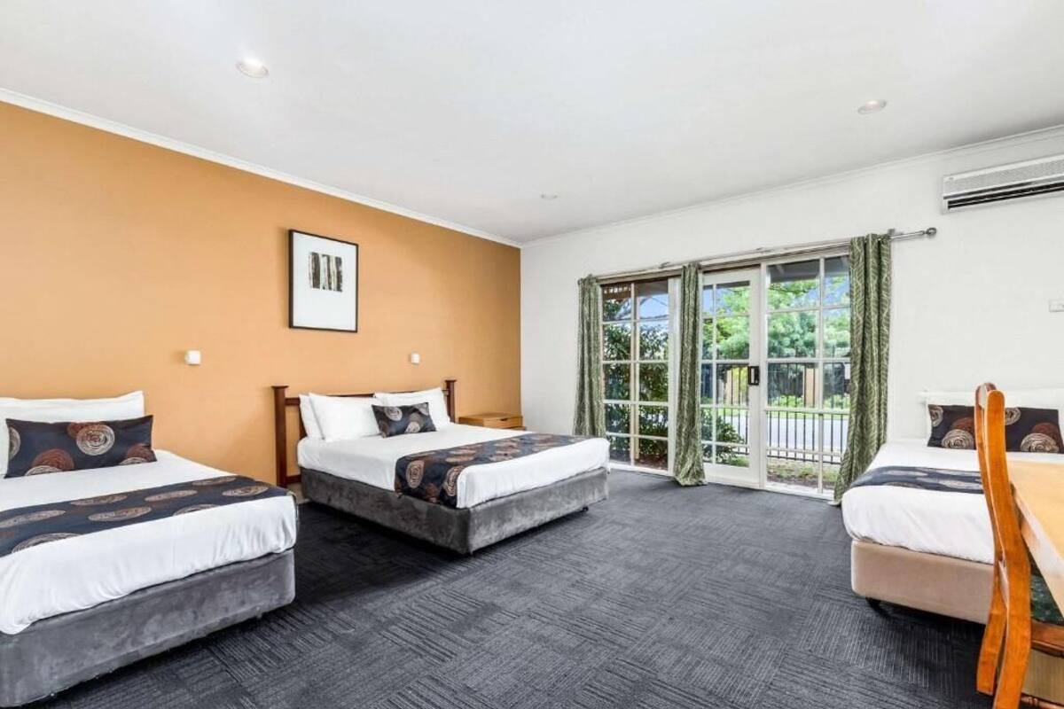 A hotel room with three beds, a large window with curtains, and a picture on the wall.
