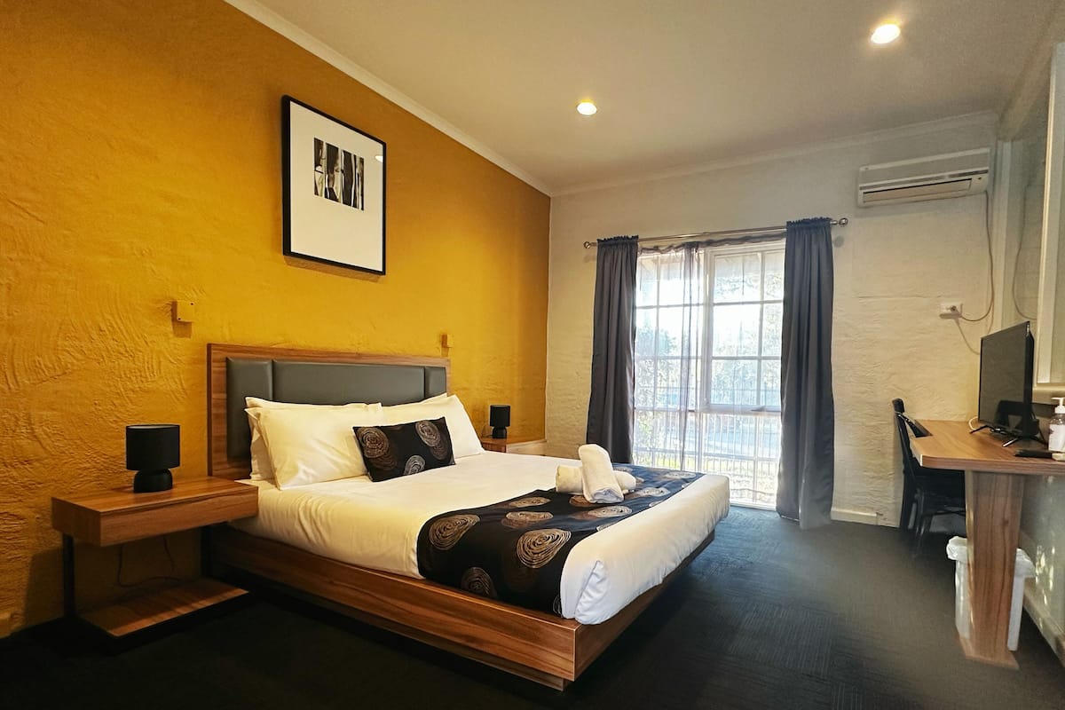 A hotel room with a large bed, a desk with a computer, and a window with curtains.