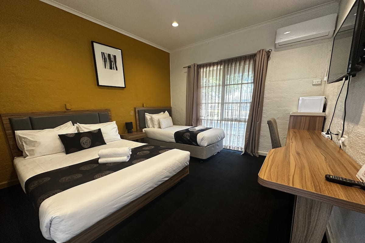 A hotel room with two beds, a wooden desk, a TV, and a window with curtains.