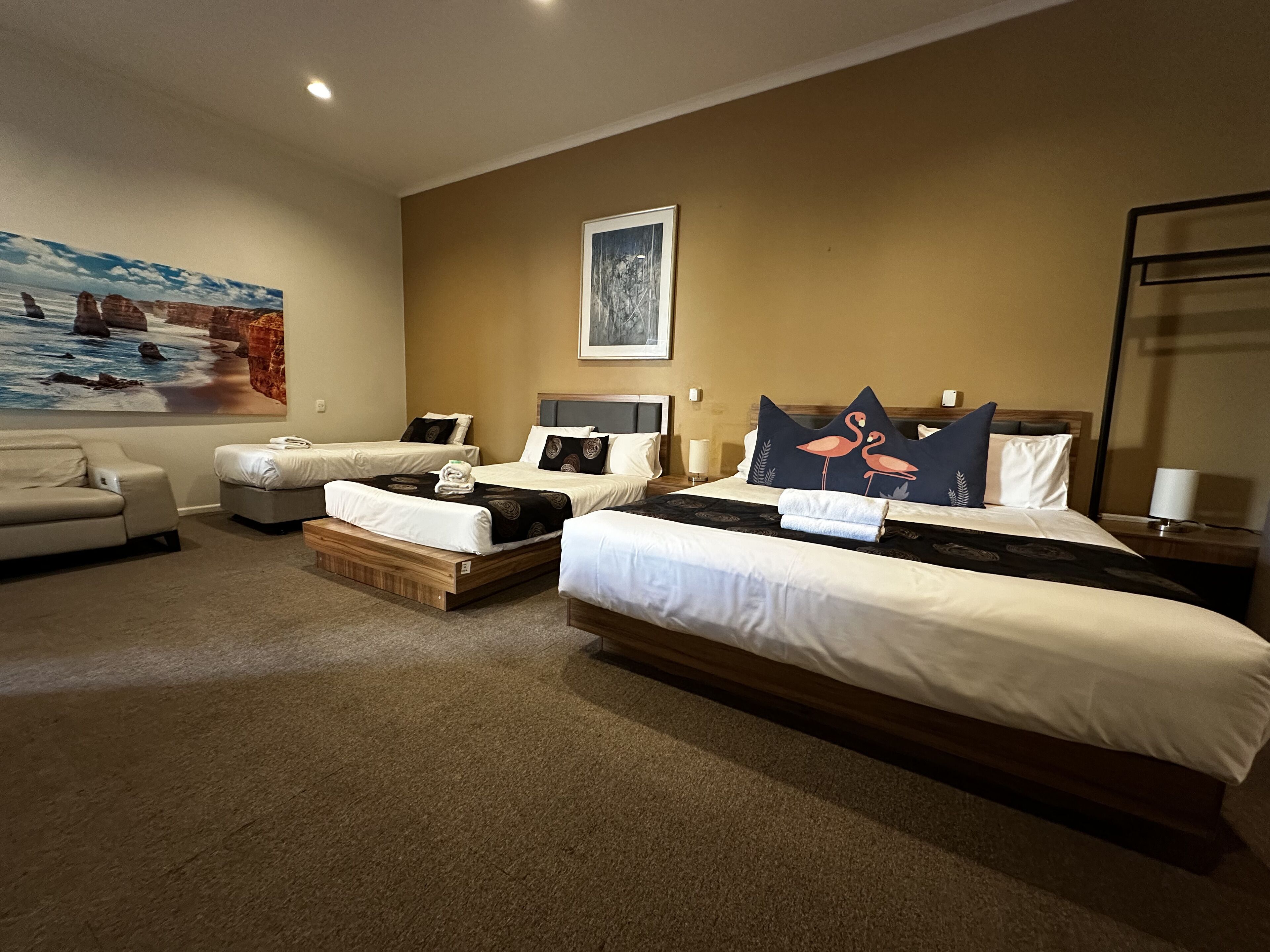 A hotel room with three beds, a sofa, and a painting on the wall.