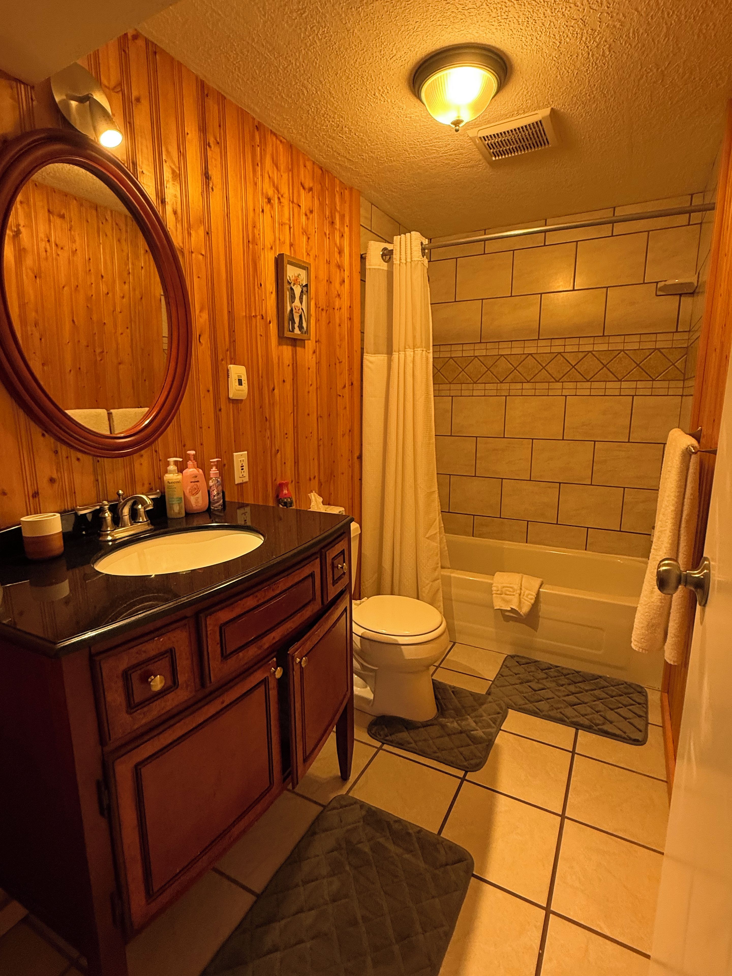 Un baño con tocador de madera, lavamanos, inodoro, bañera y cortina de ducha.