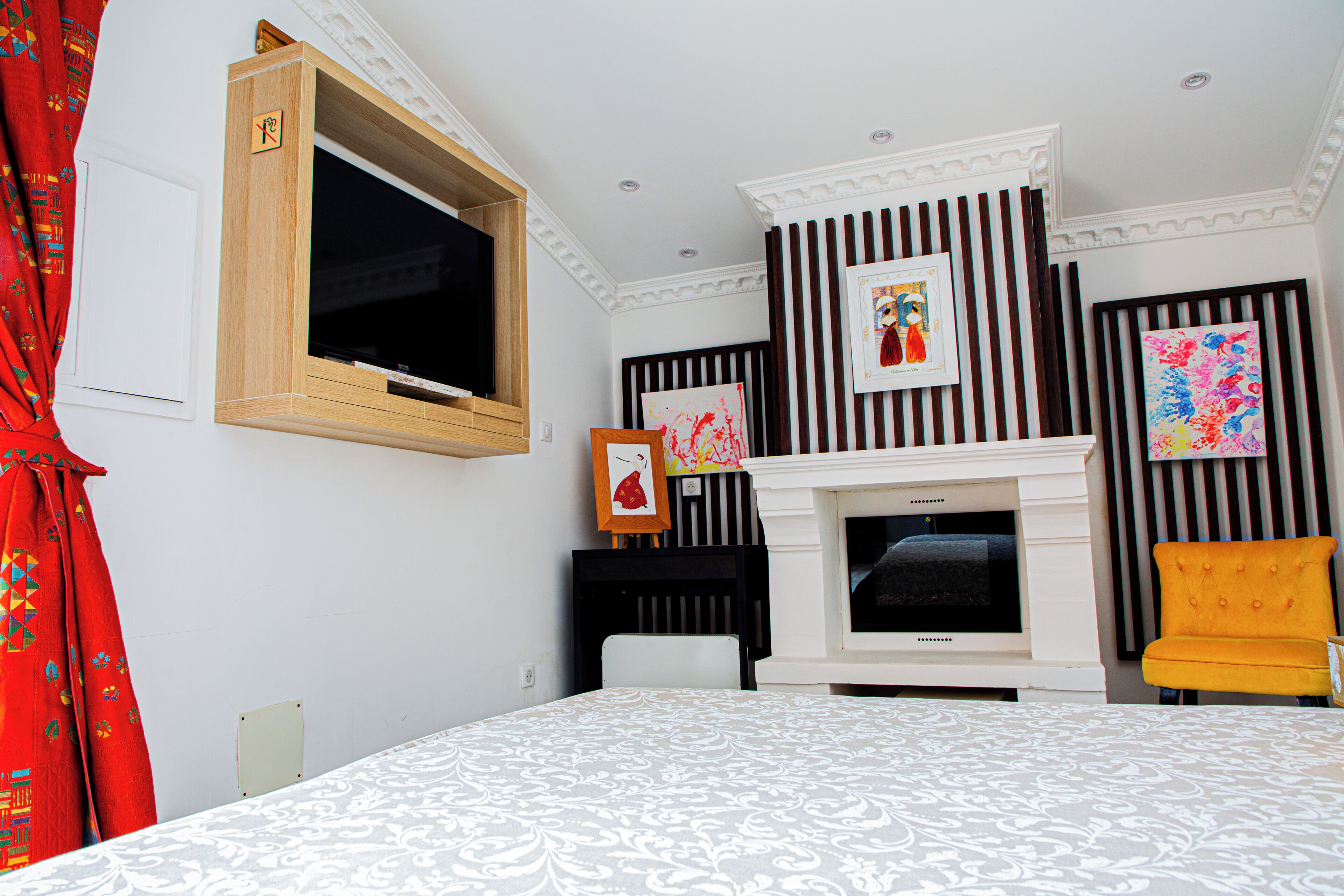 A hotel room with a bed, a television, a fireplace, and artwork on the walls.