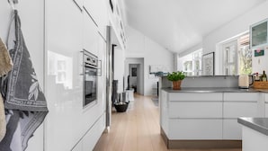 A modern kitchen with white cabinetry, a built-in oven, and a large island with a sink. - Cozy home in Vejby with sauna (Vejby)