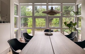 A dining area with a wooden table, black chairs, a hanging light fixture, and large windows with a view of greenery. - Cozy home in Vejby with sauna (Vejby)