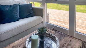 A sofa with cushions, a tray with a candle and a succulent plant, and a view of a wooden deck through large windows. - Cozy home in Vejby with sauna (Vejby)