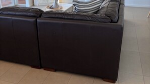 Ein modernes Wohnzimmer mit einem Ecksofa, einem Flachbildfernseher und einem großen Fenster mit Jalousien.