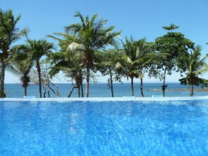 Ein klares, blaues Schwimmbecken mit Palmen und Blick aufs Meer.