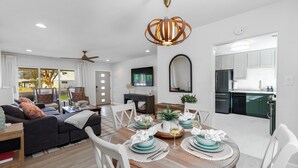 A modern living room with a dining area, white walls, and a kitchen in the background.