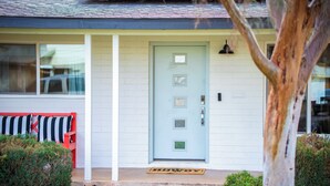 A house with a light blue door, a red bench, and a doormat.