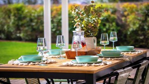 A dining table set with teal bowls, wine glasses, and a pitcher, surrounded by greenery.