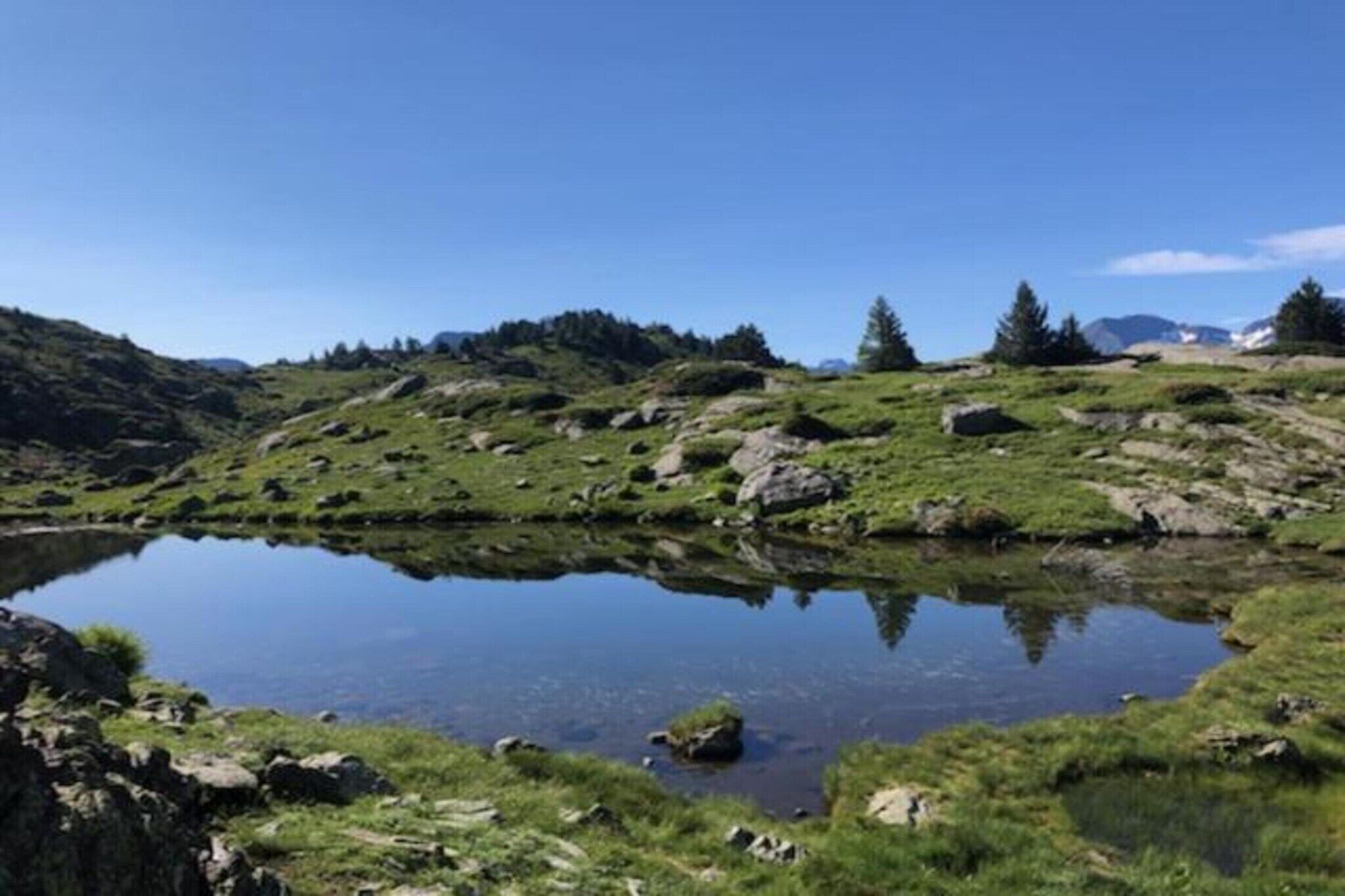 A serene landscape with a clear lake surrounded by grassy hills and scattered rocks.