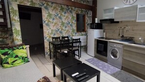 Una cocina compacta con lavadora, microondas y fregadero. Hay una zona de comedor con mesa y sillas.