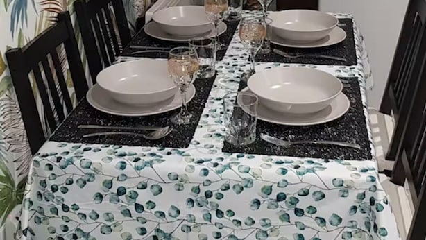 Una mesa de comedor lista con platos, vasos y cubiertos, rodeada de sillas.