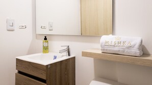 Un bagno con un mobiletto portaoggetti in legno, un lavandino bianco, uno specchio, un asciugamano con la scritta "MISHKA" e un water.