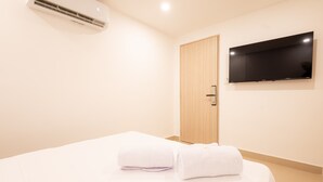 Una camera d'albergo con un letto, una TV a muro e un condizionatore d'aria.