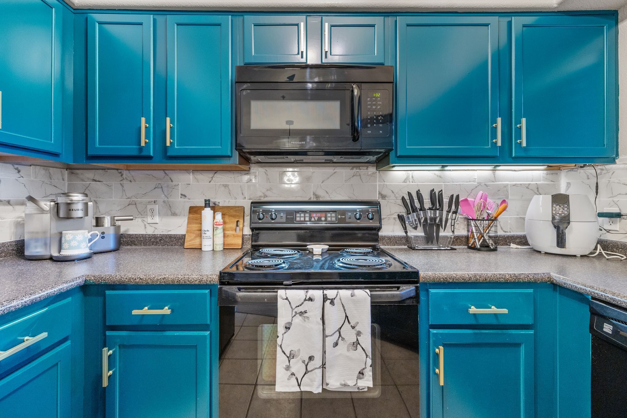 A kitchen with teal cabinets, a stainless steel microwave, a stove, and various kitchen appliances.