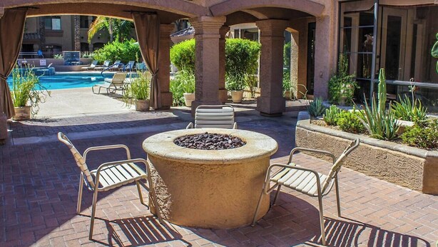 An outdoor patio with a fire pit, lounge chairs, and a pool in the background. - Kid Friendly 2-bedroom condo in Scottsdale with Pool, Hottub, fitness room, WiFi (Scottsdale)