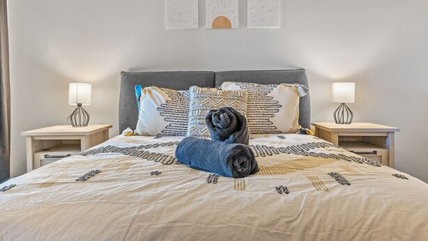 A neatly made bed with patterned bedding, two bedside lamps, and decorative wall art. - Kid Friendly 2-bedroom condo in Scottsdale with Pool, Hottub, fitness room, WiFi (Scottsdale)