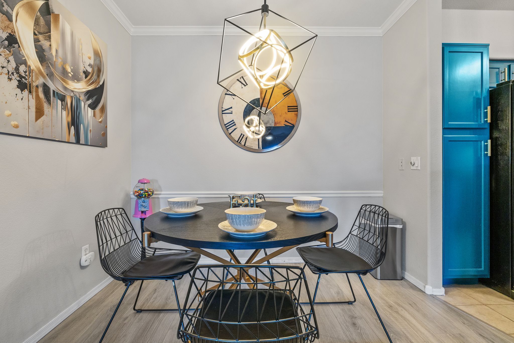 Un coin repas avec une table ronde, des chaises noires et une horloge au design original accrochée au mur.