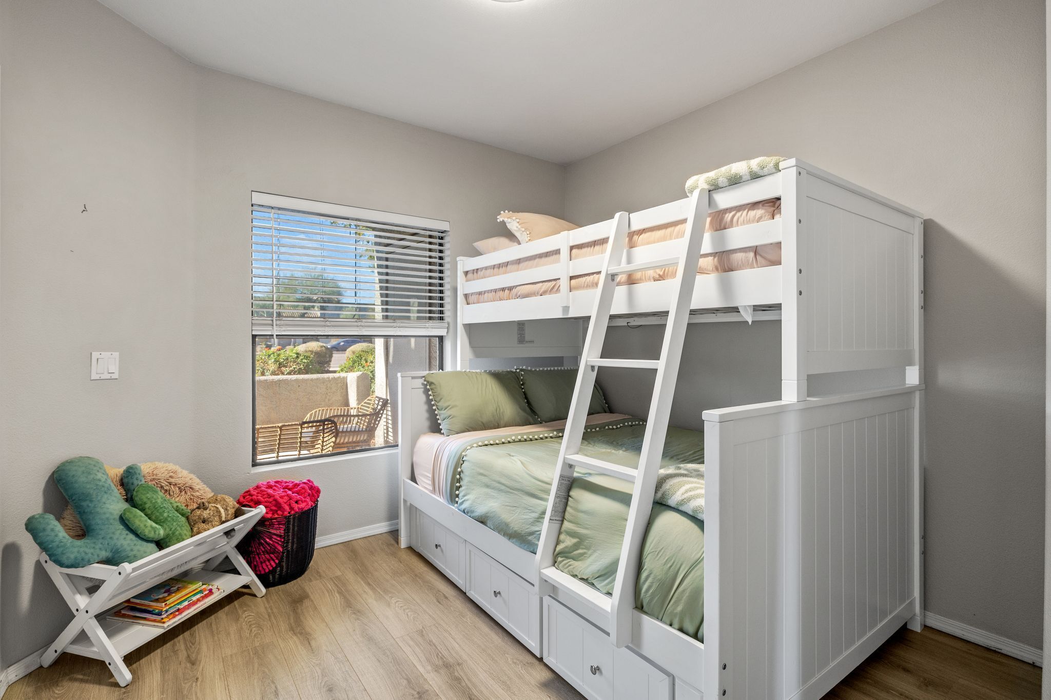 A bunk bed room with a window, a small table with books, and a chair.